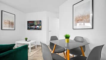 Una habitación moderna con una mesa de comedor, sillas, un sofá verde, una pequeña mesa blanca con una planta y dos obras de arte enmarcadas en las paredes.