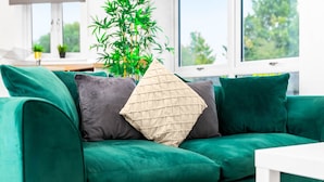 Een groene bank met twee kussens, een witte tafel en een bamboeplant in een kamer met een raam.