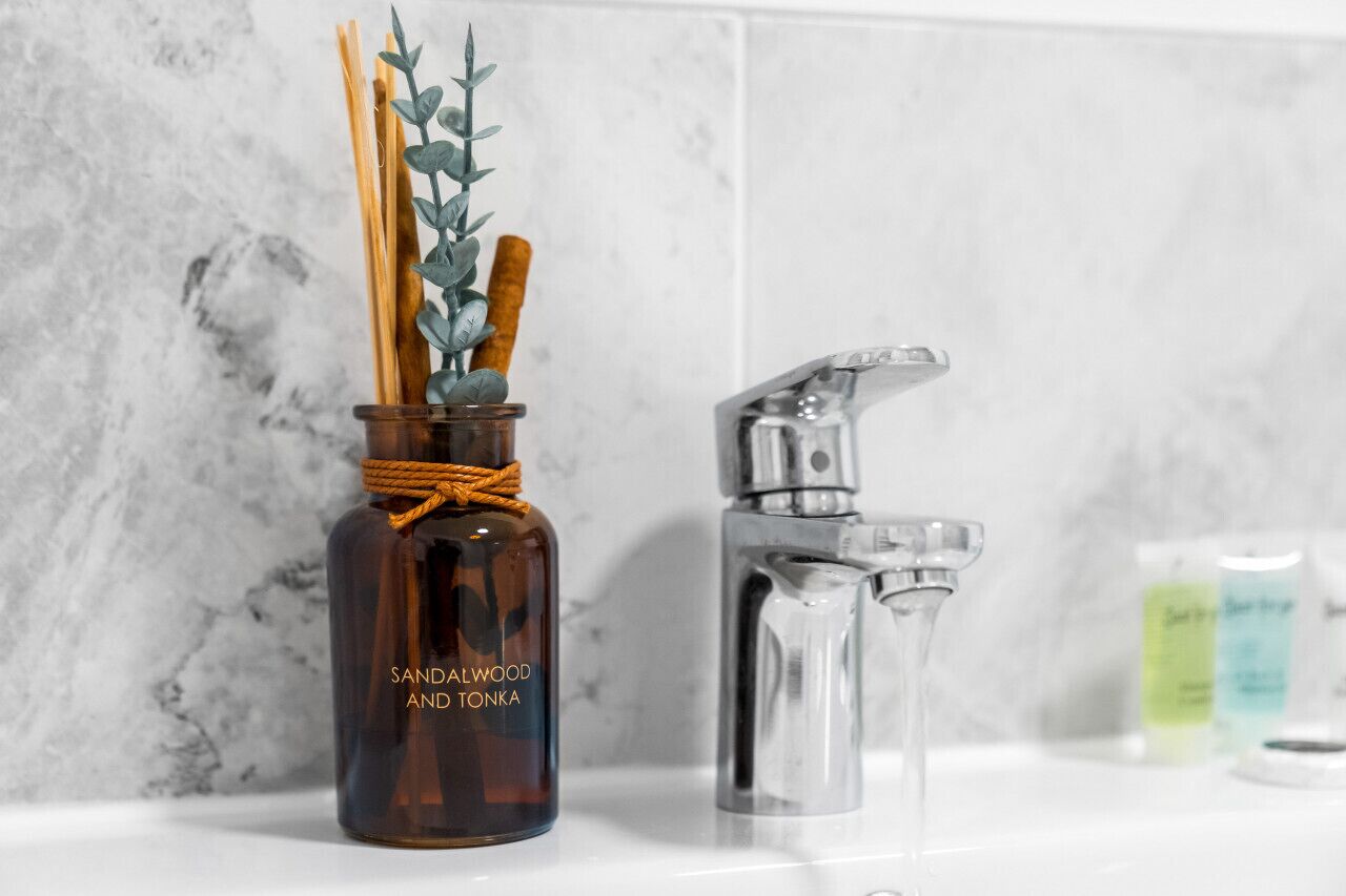 Een badkamer met een donkerbruine fles met de tekst 'Sandelhout en Tonka' en een heldere spuitfles.