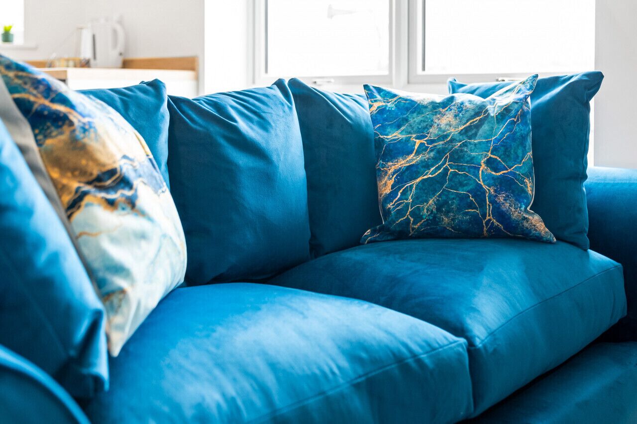 A blue sofa with matching cushions in a bright room with a window.