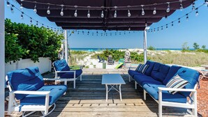 Een terras met houten vloer, blauwe zitkussens, een witte tafel en een overdeeld gedeelte met lichtslingers.