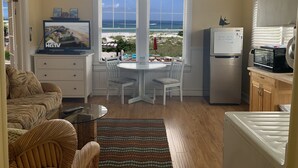 Cozinha compacta com área de refeições, geladeira, micro-ondas e vista para o oceano.