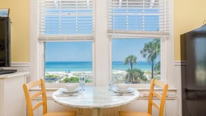 Uma sala de jantar com mesa e cadeiras, vista para a praia e uma televisão à esquerda.