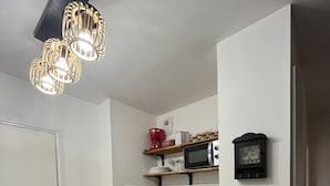 Eine kompakte Küche mit Mikrowelle, Spüle und einem kleinen Mülleimer. Darüber befinden sich Regale mit verschiedenen Küchenutensilien.