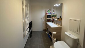 Ein kleines Badezimmer mit Toilette, Waschbecken und Spiegel. Handtuchhalter und Ablagefläche für Toilettenartikel vorhanden.