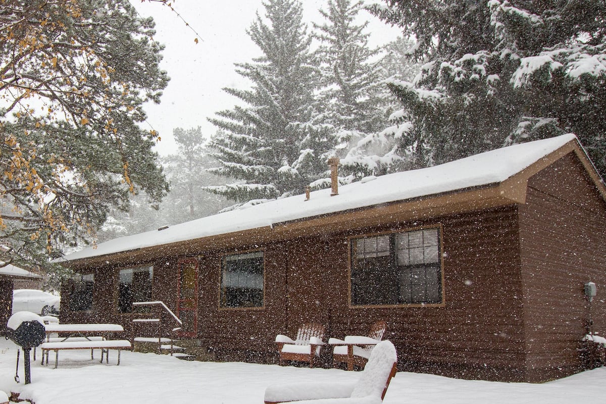 A cabin with a snow-covered roof, wooden exterior walls, and a front porch with benches.