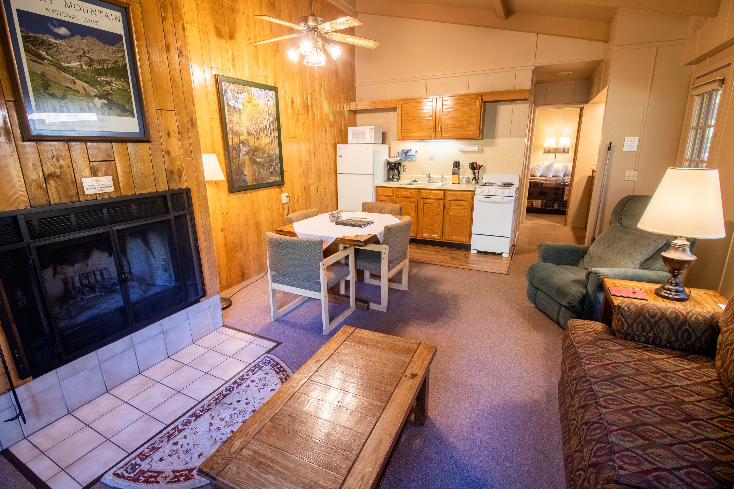 Una sala de estar acogedora con chimenea, paredes de madera, un comedor y una cocina al fondo.