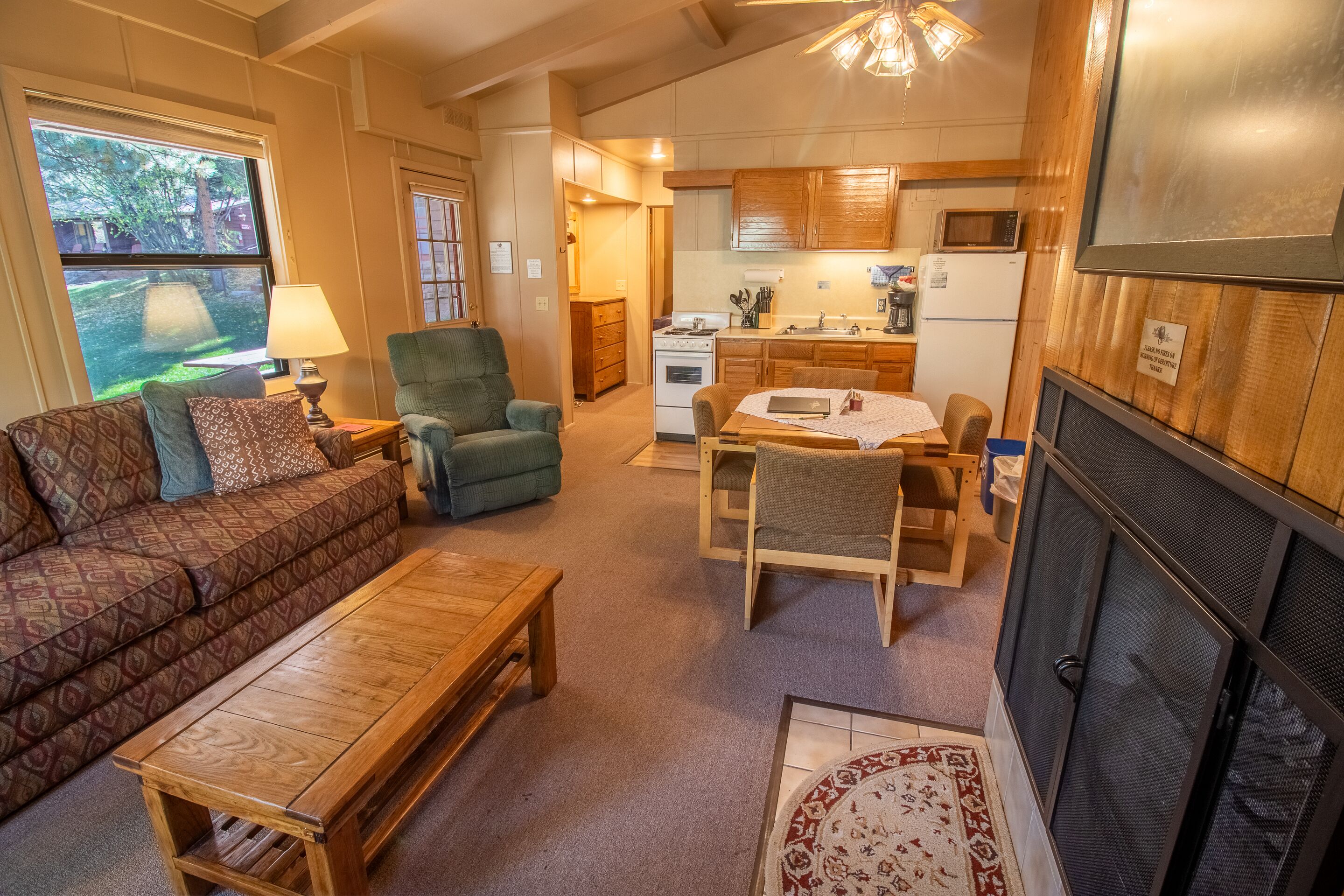 A cozy living room with a sofa, armchair, and coffee table, a dining area with a table and chairs, and a kitchen with wooden cabinets and appliances.