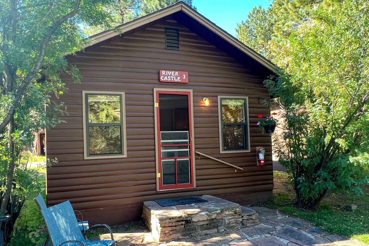 A wooden cabin labeled "River Castle 3" with a red door, two windows, and a small porch area.