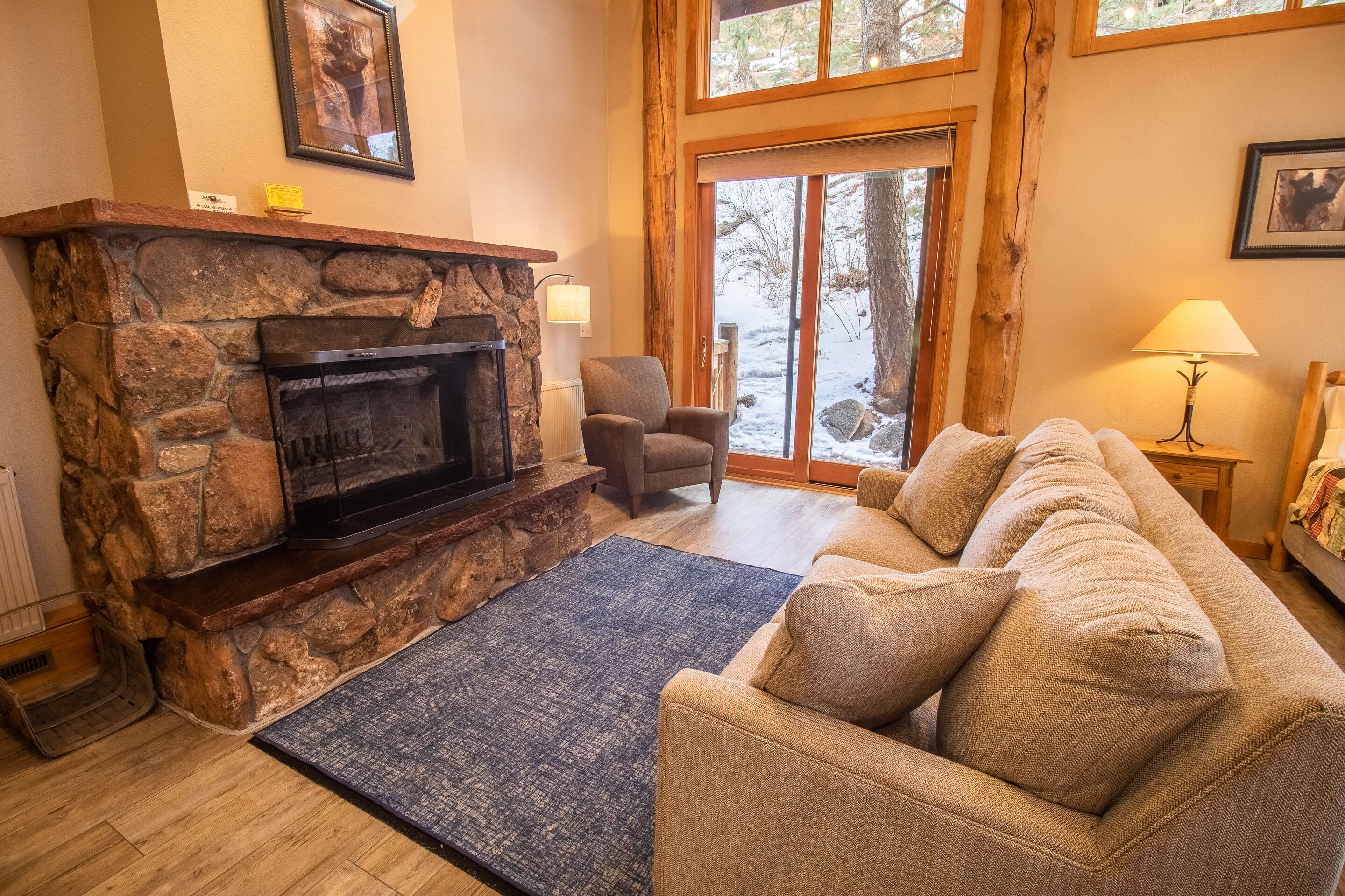 A cozy living room with a stone fireplace, a comfortable sofa, and a view through a glass door.
