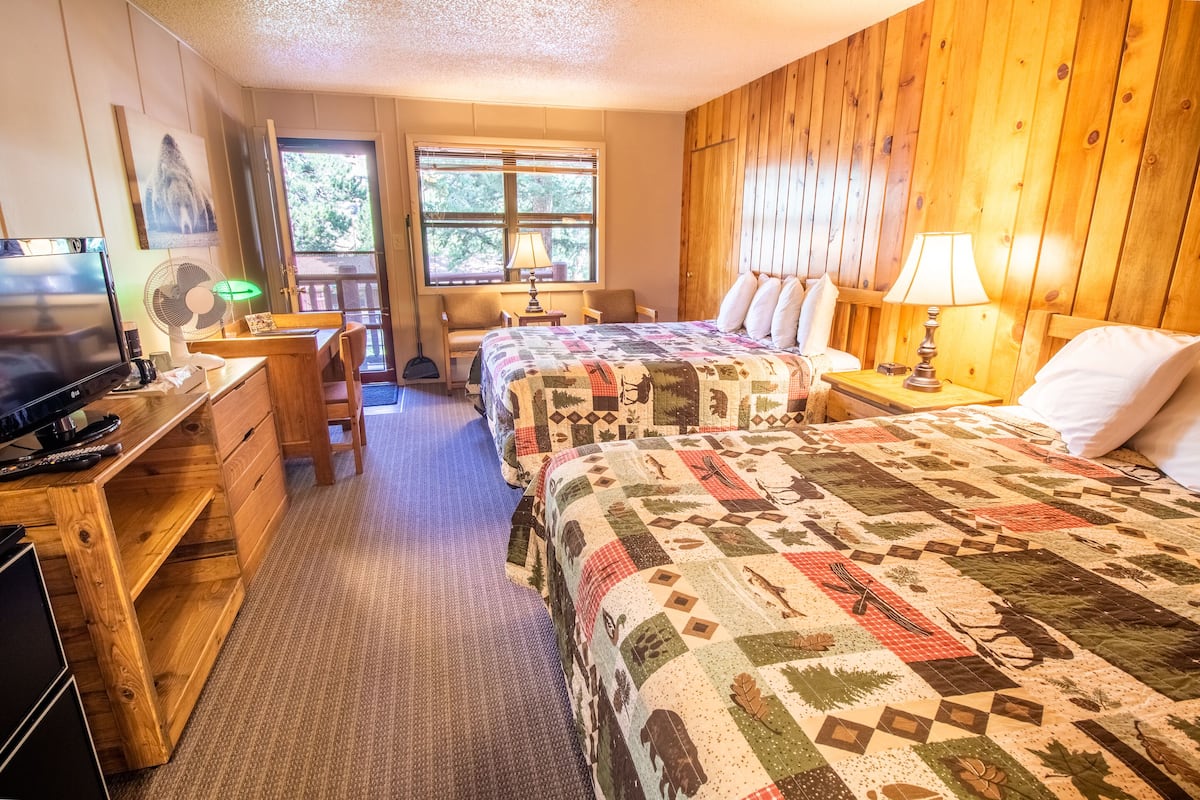 A cozy room with two beds, a desk with a computer, a TV, and a window with blinds.