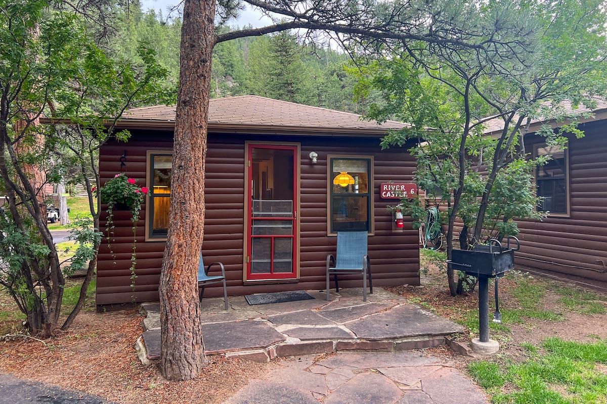 A rustic cabin with a red door, a small porch, and a sign reading "River Castle 6".