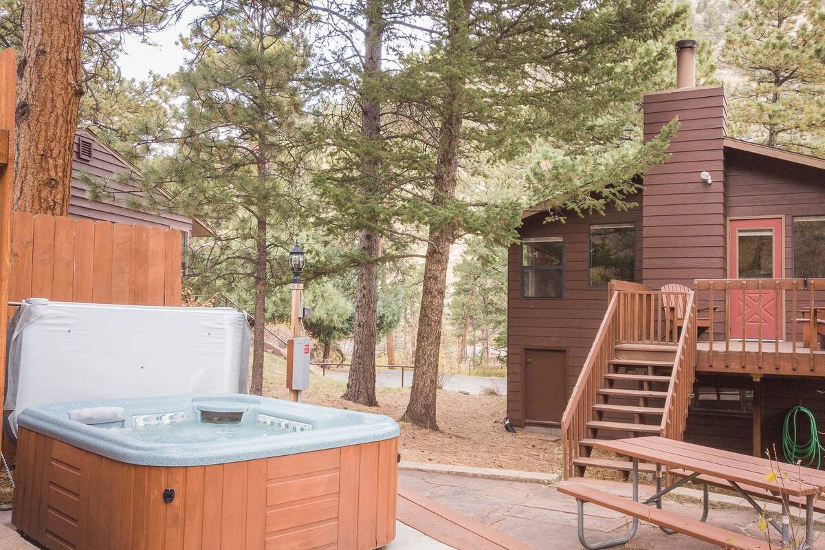A wooden cabin with a hot tub, deck, and stairs leading to a loft area.