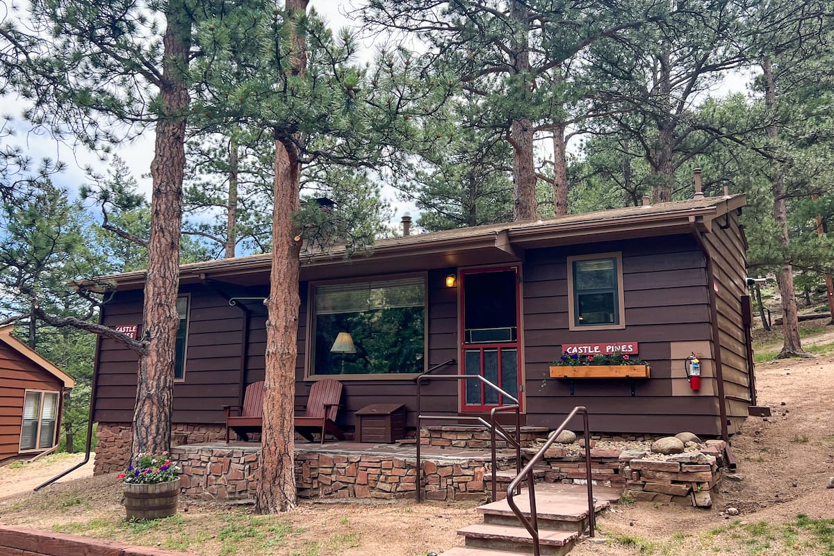A rustic cabin with a stone foundation, wooden exterior, and a sign reading "Castle Pines."
