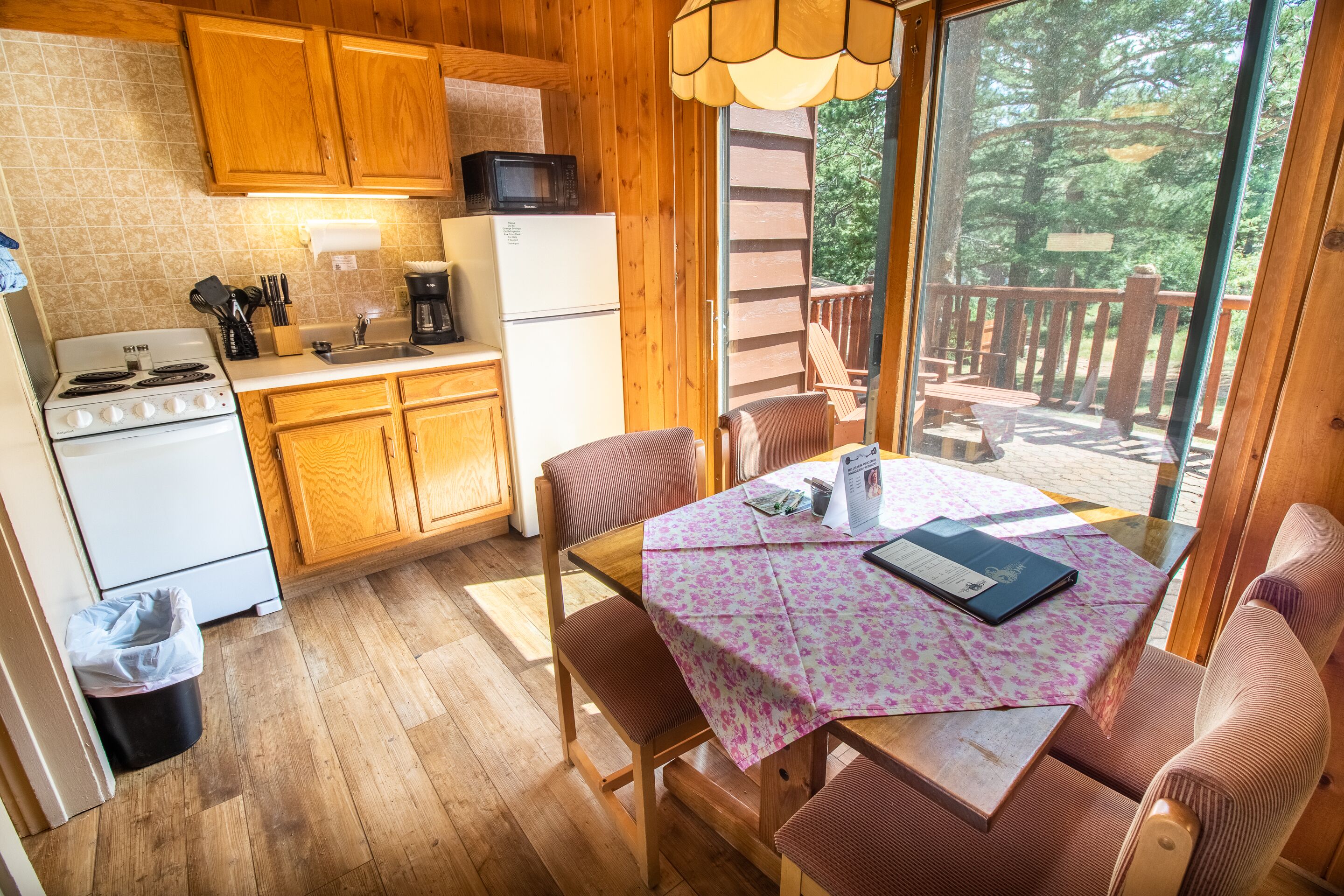 Una cocina con armarios de madera, estufa y refrigerador. Hay una mesa de comedor con mantel rosa con estampado floral y sillas.