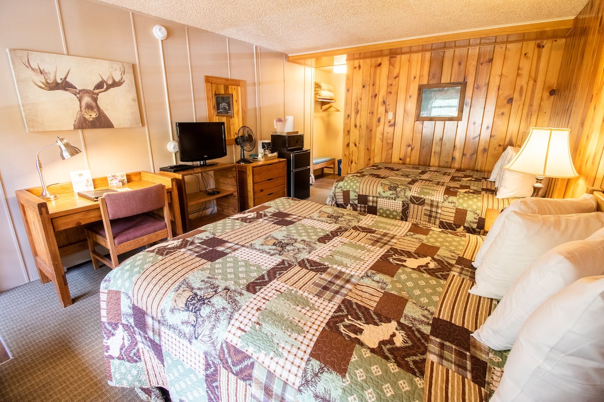 A hotel room with two beds, a desk with a computer, a television, and a wooden wall with a mounted picture.