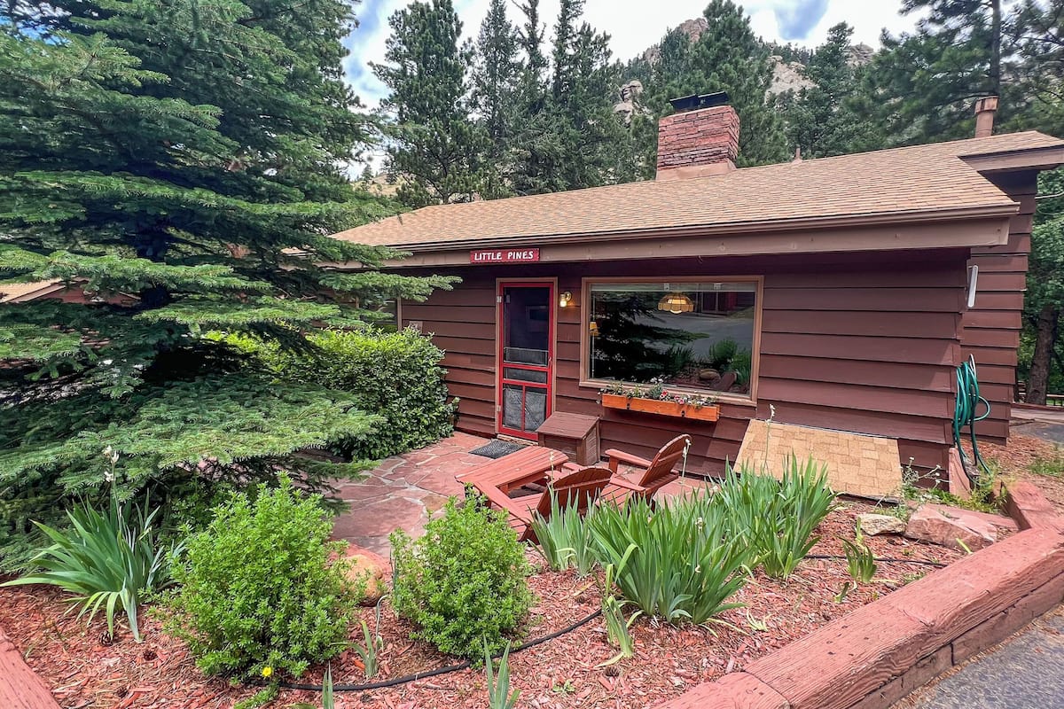 A small cabin with a red door, a window, and a sign that reads "Little Pines."