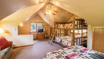 Une chambre mansardée chaleureuse avec des lits superposés, un bureau et un ventilateur de plafond.
