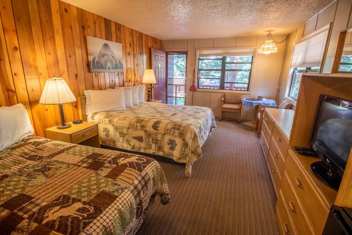 A room with two beds, a television, a desk, and a window with a view of the outdoors.