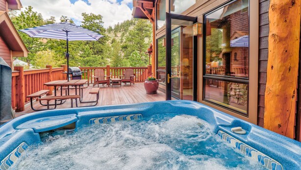 A wooden deck with a hot tub, outdoor furniture, and a glass door leading to a patio area. - Castle Mountain Lodge (Estes Park)