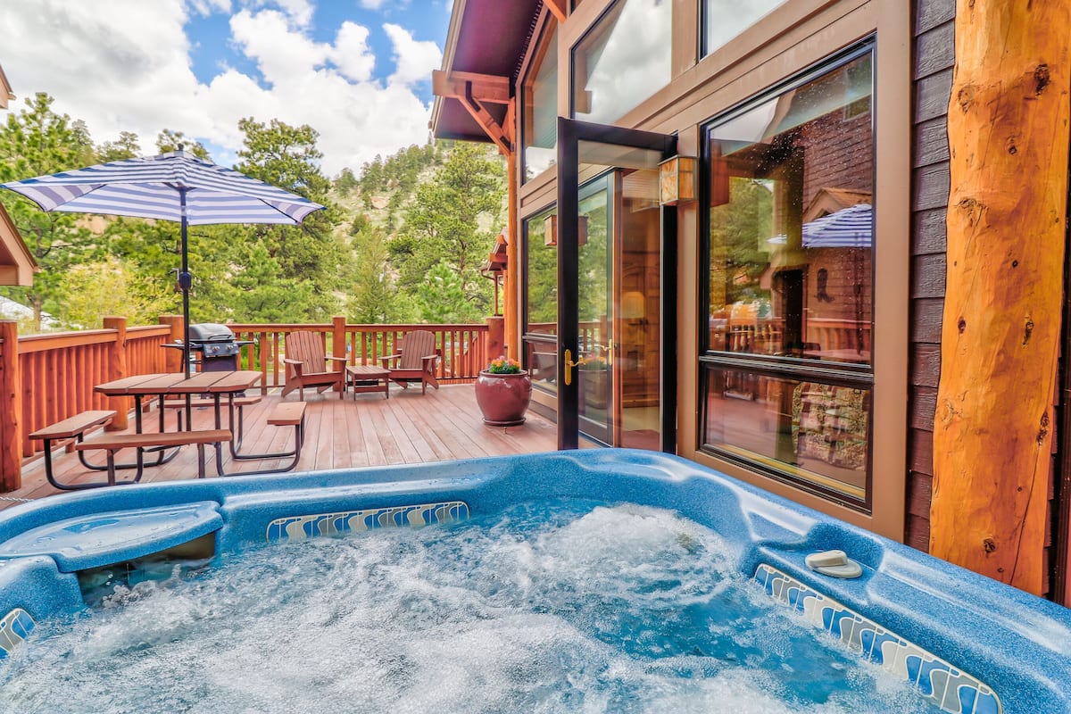 A wooden deck with a hot tub, outdoor furniture, and a glass door leading to a patio area.