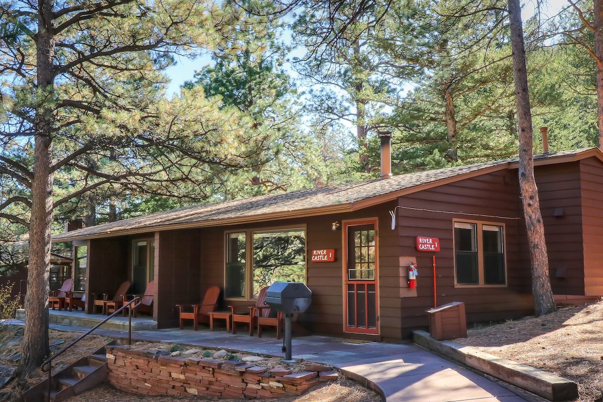 A rustic cabin with a covered porch, outdoor seating, and a sign reading "River Castle."