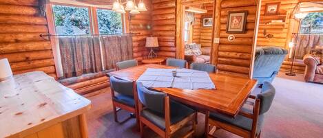 Een gezellig blokhutinterieur met een eethoek, twee stoelen, een tafel met placemat en een lamp.