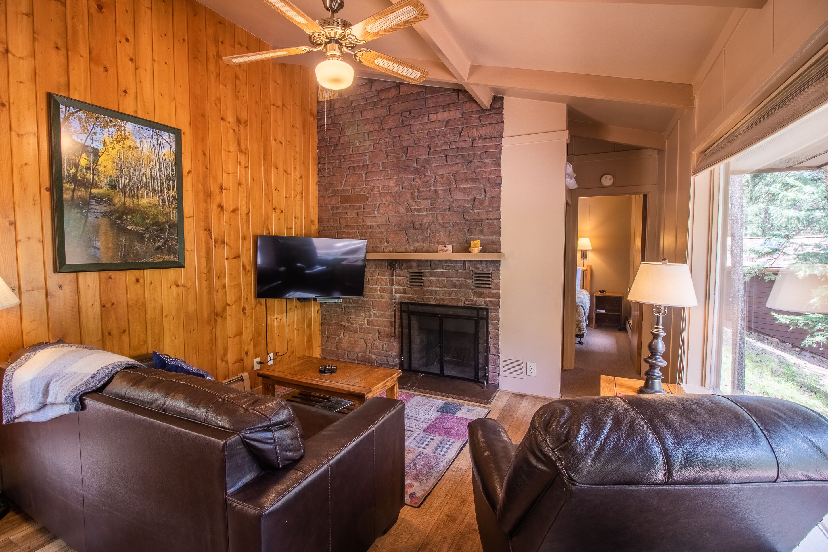 A cozy living room with a fireplace, leather sofas, a flat-screen TV, and wooden walls.