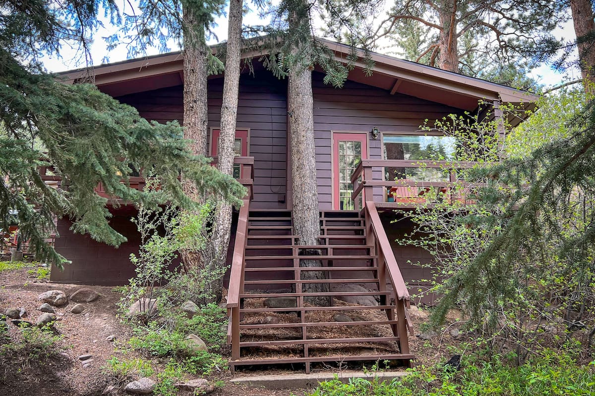 A cabin with a wooden staircase leading to a deck, surrounded by trees.