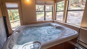A hot tub with a digital temperature gauge, surrounded by windows with blinds, in a room with a door and a light fixture. - Castle Mountain Lodge (Estes Park)