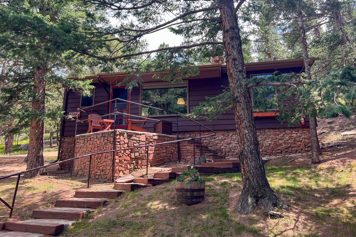 A rustic cabin with a stone foundation, wooden exterior, and a staircase leading to a deck.