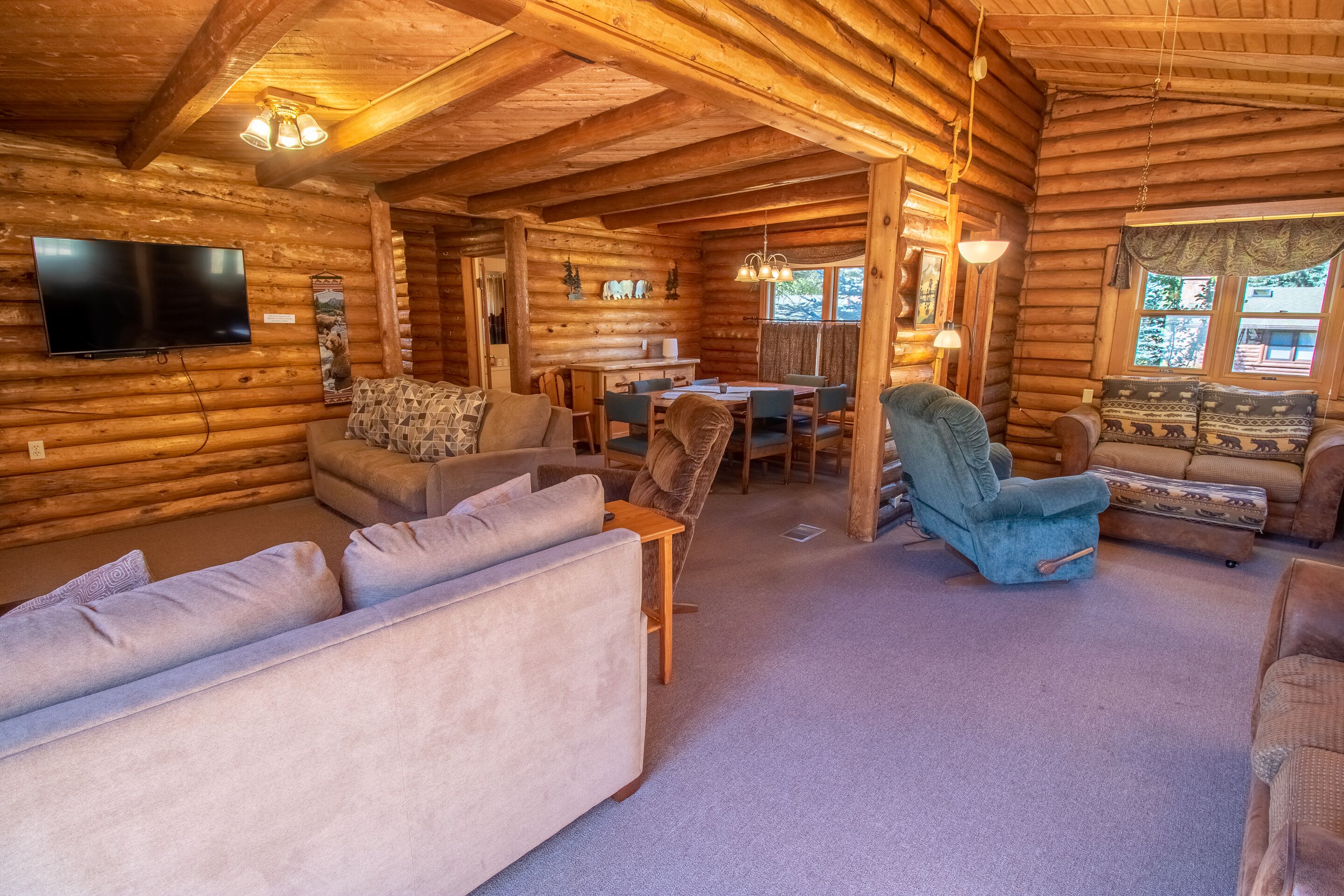 A log cabin interior with a living room, dining area, and a TV mounted on the wall.