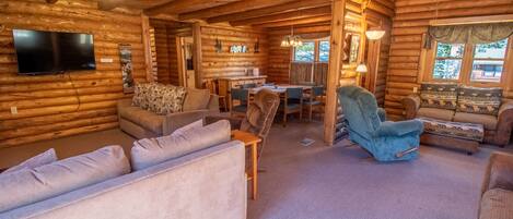 A log cabin interior with a living room, dining area, and a TV mounted on the wall.