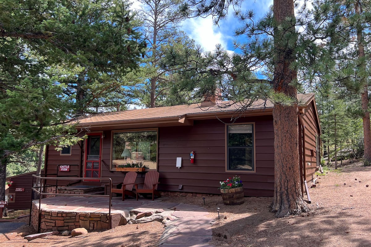 A cabin with a stone foundation, wooden deck, and a red door.