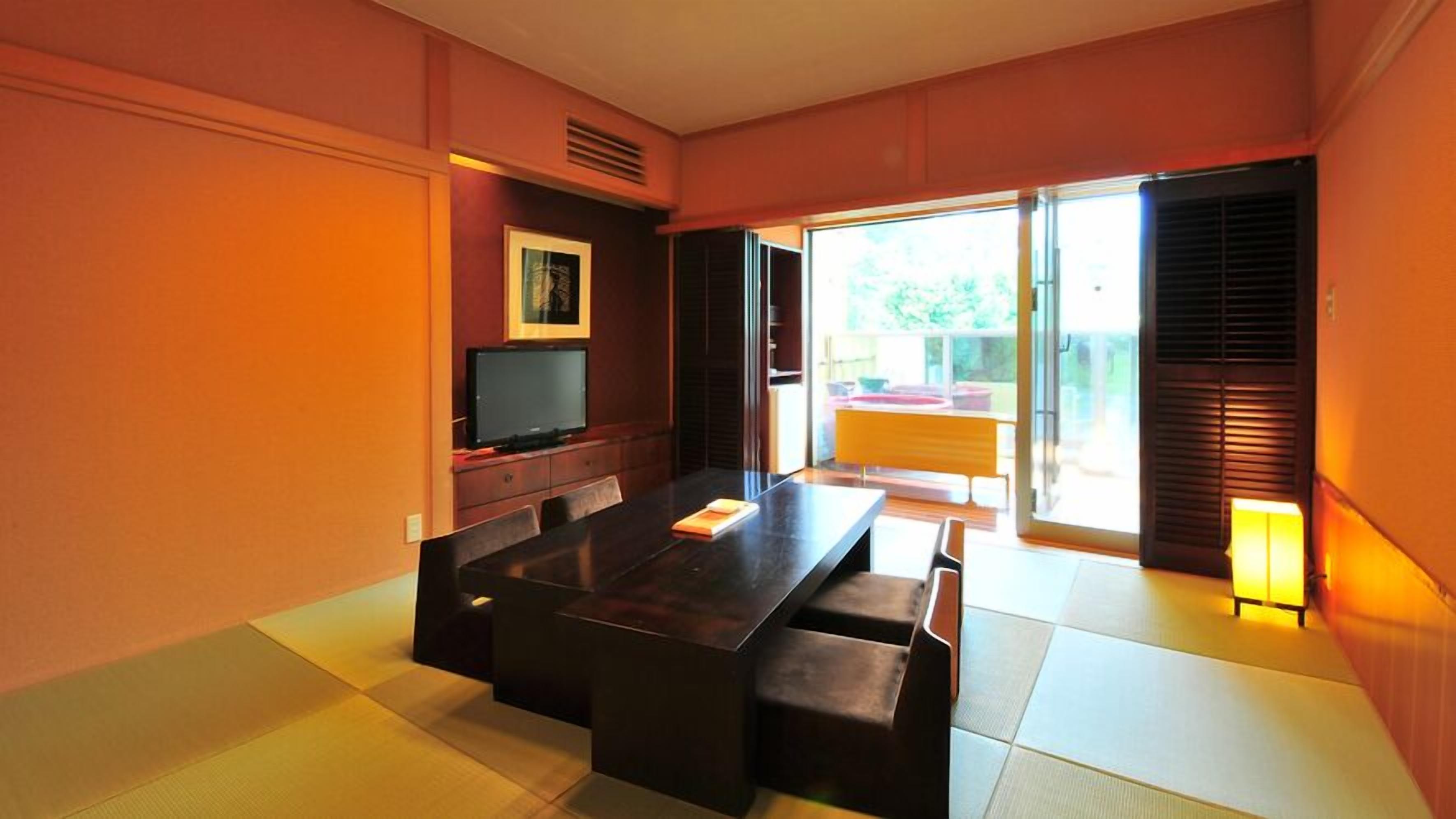 A modern room with a large black table, a flat-screen TV, and a sliding glass door leading to an outdoor area.