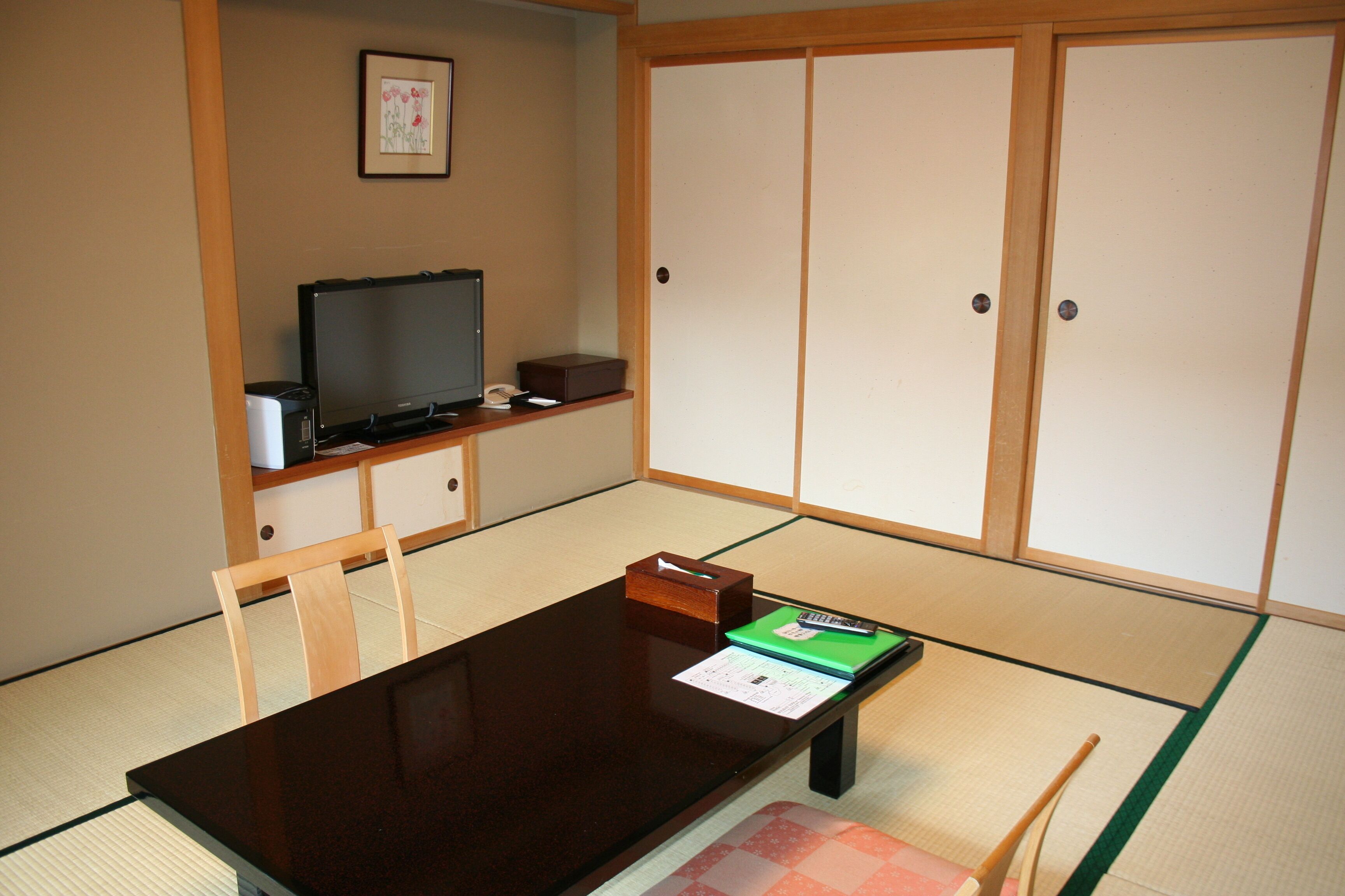 A traditional Japanese room with tatami flooring, a low table, a television, and sliding doors.