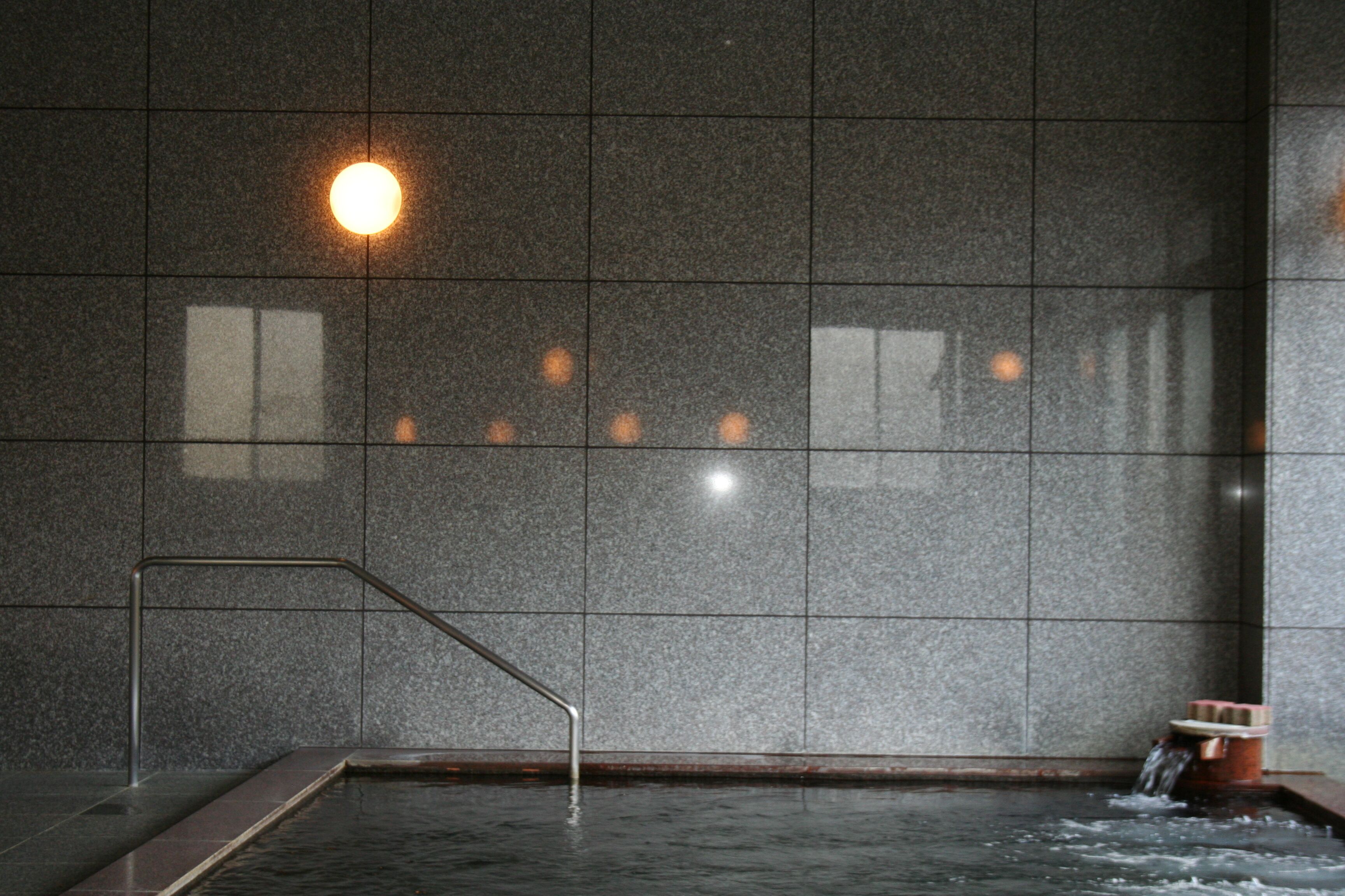 A spa area with a tiled wall, a metal handrail, a small water feature, and a light fixture.