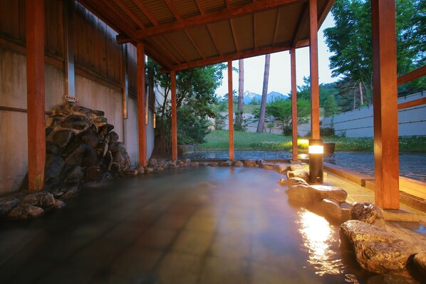 A traditional Japanese onsen with a wooden structure, a stone wall, and a view of mountains.