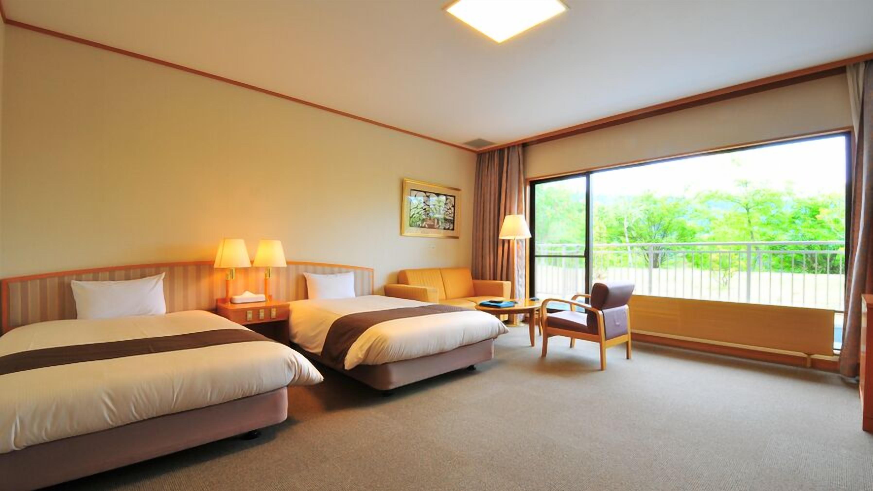 A hotel room with two beds, a small table, a chair, and a balcony with a view.