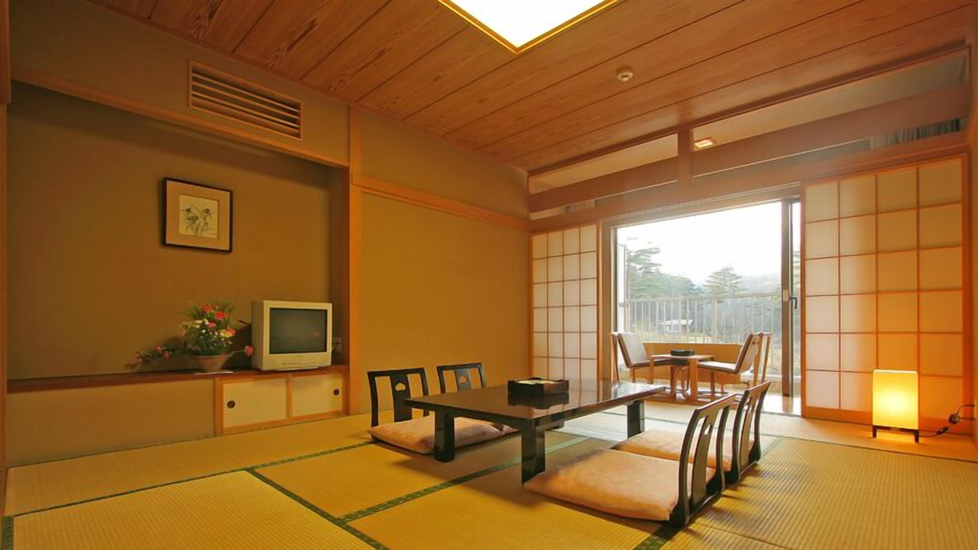A traditional Japanese room with tatami flooring, a low table, chairs, a television, and sliding doors leading to a balcony.