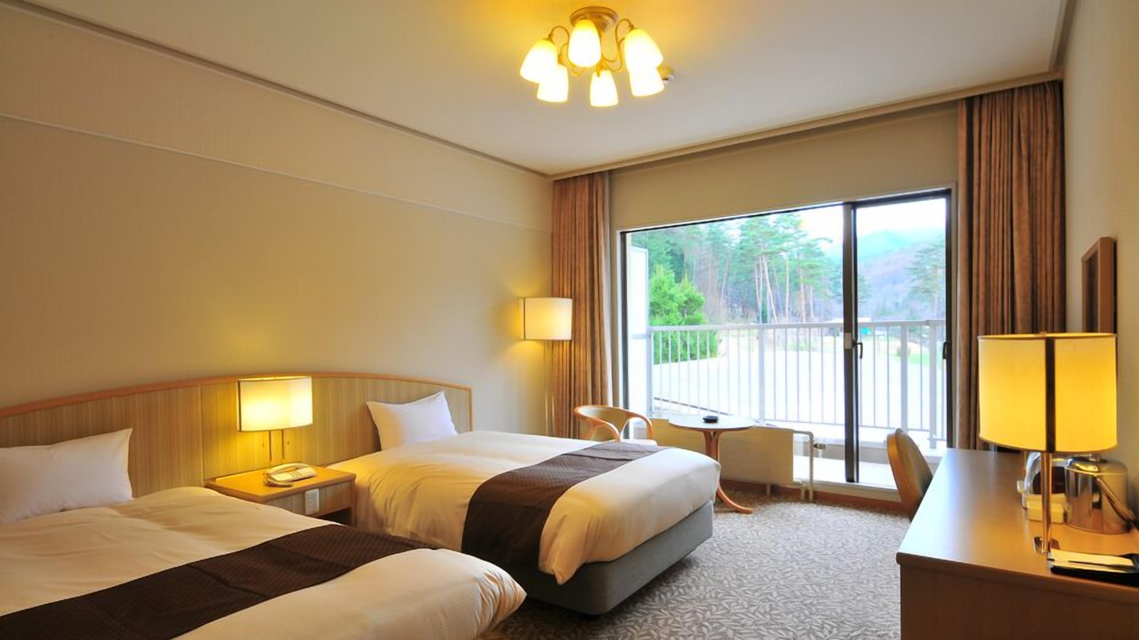 A hotel room with two beds, a desk, a chair, a balcony with a view, and a chandelier.