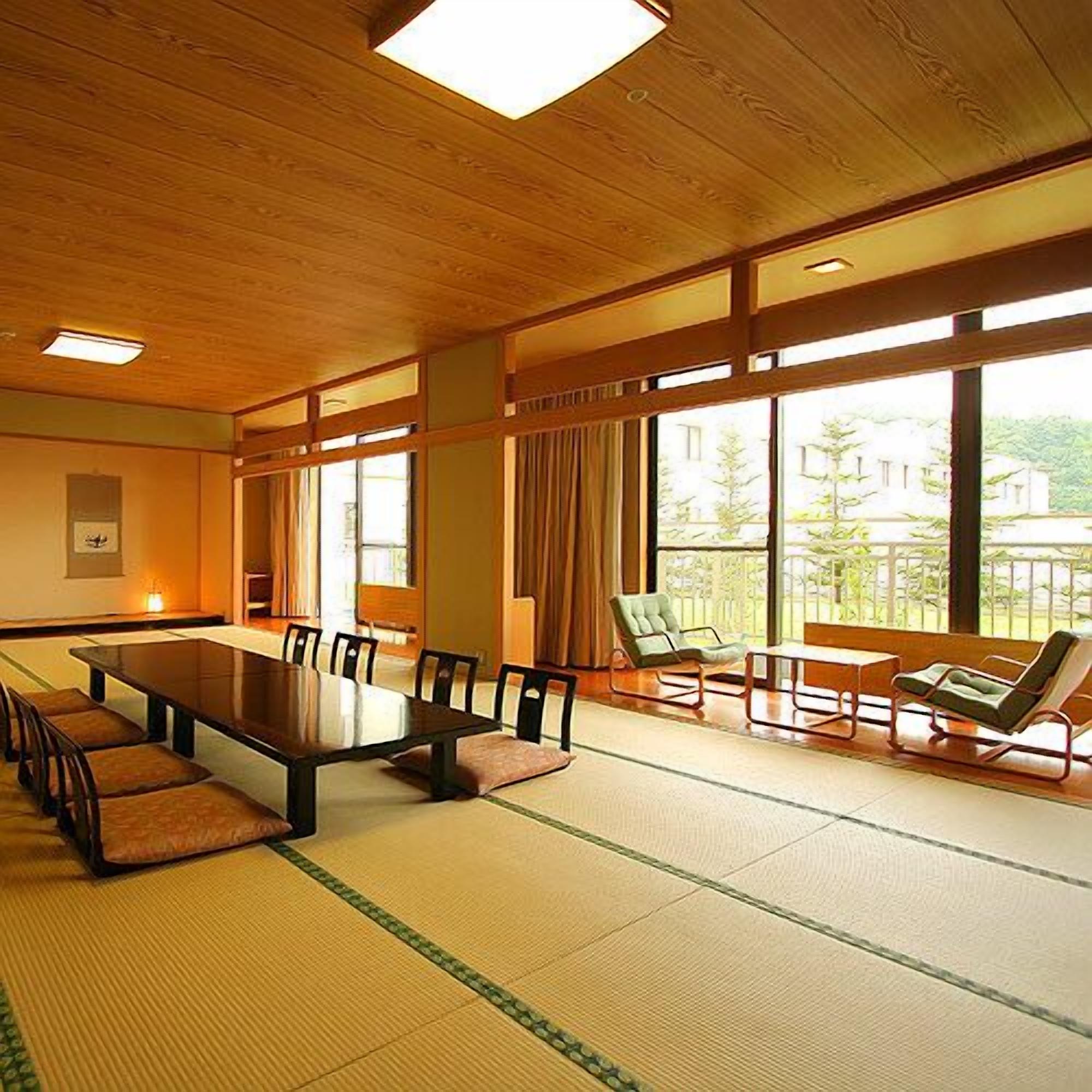 A room with tatami flooring, a long table, chairs, and a sofa.