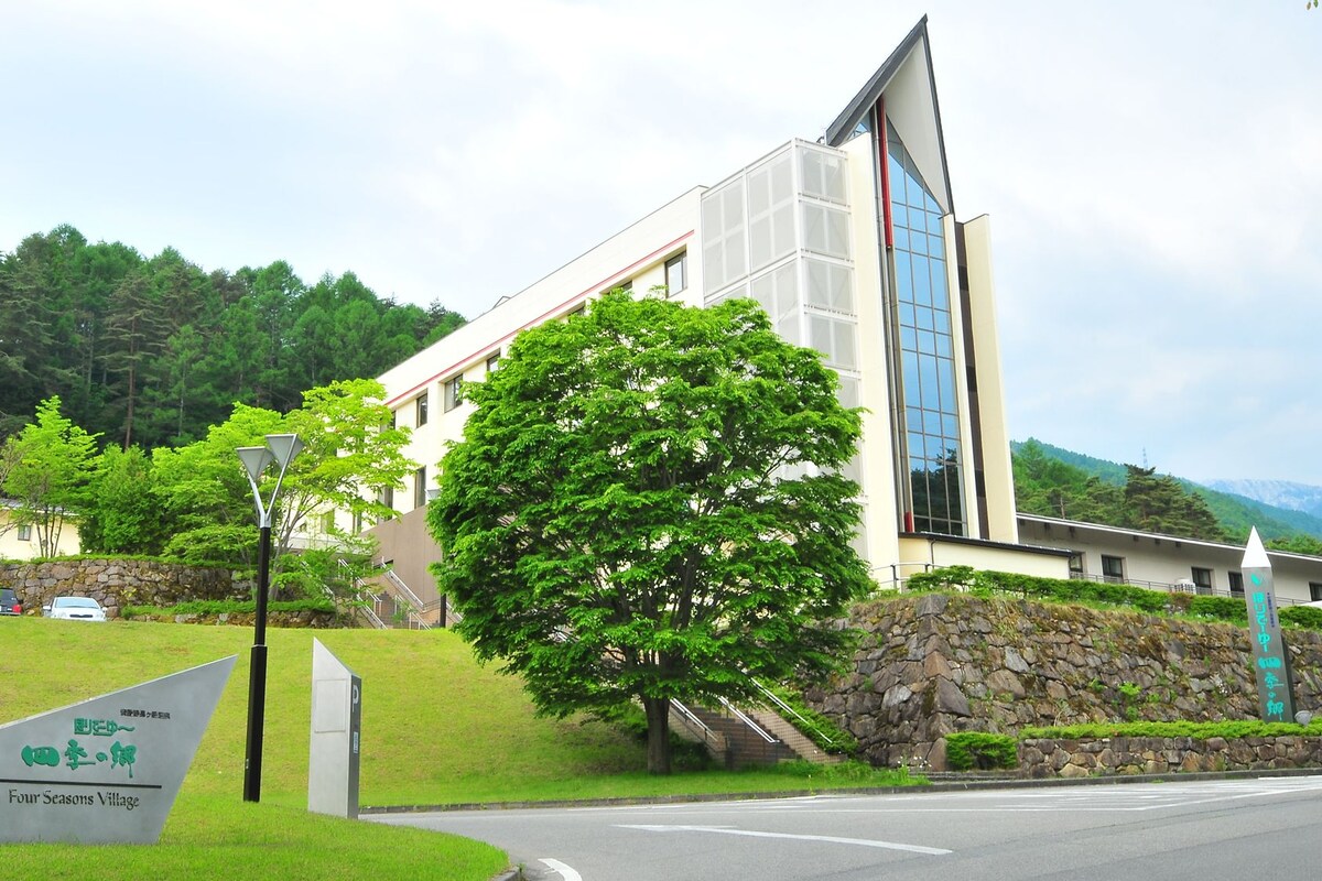 Un edificio moderno con fachada de vidrio, rodeado de vegetación y un muro de piedra.