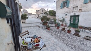 A courtyard with a table set for tea, surrounded by potted plants and stone flooring. - Yellow gecko--in the heart of the stones (Matera)