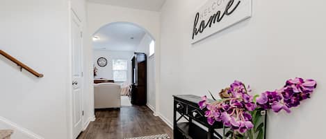 A hallway with a welcome sign, a staircase, and a console table with purple flowers.