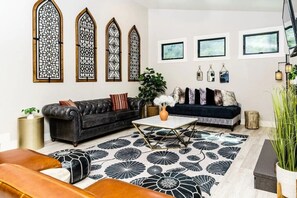 A living room with a black leather sofa, a coffee table, and a patterned rug. - Poppy Cottage Home 4BR (Carlsbad)