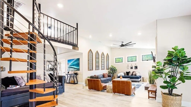 A spacious living area with a modern staircase, a ceiling fan, and a large potted plant. - Poppy Cottage Home 4BR (Carlsbad)
