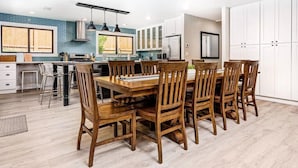 A modern kitchen with a dining area, featuring a large wooden table and chairs, white cabinets, and a blue backsplash. - Poppy Cottage Home 4BR (Carlsbad)