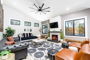 A modern living room with a fireplace, leather sofas, and a large TV. - Poppy Cottage Home 4BR (Carlsbad)