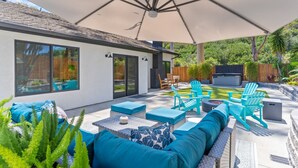 A patio with outdoor furniture, a large umbrella, and a fire pit. - Poppy Cottage Home 4BR (Carlsbad)